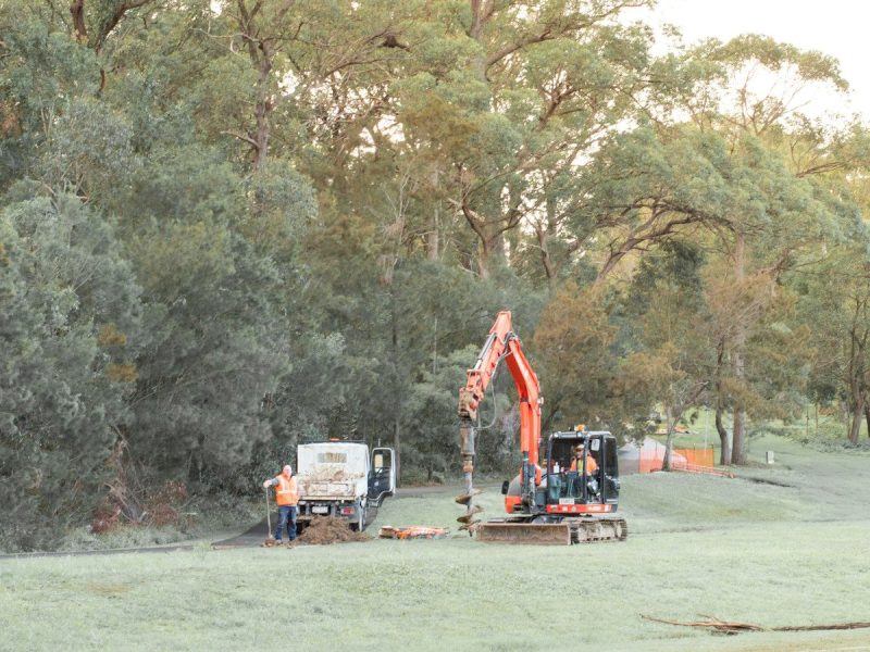 Orange excavator, utility truck, and workers in a grassy field.