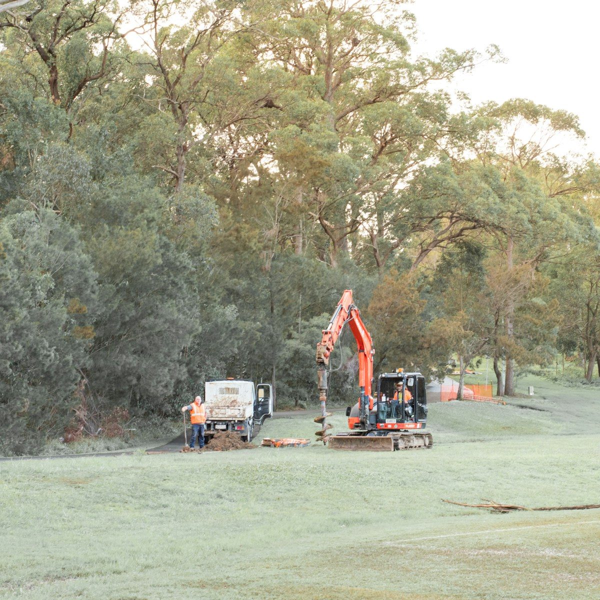 Orange excavator, utility truck, and workers in a grassy field.